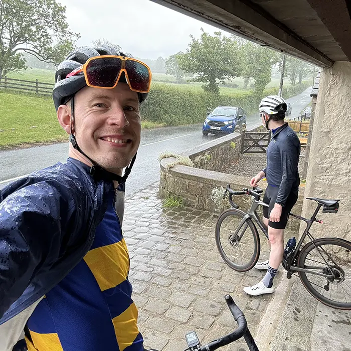 Two riders sheltering on wet cobbles in the rain