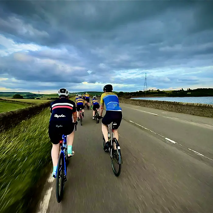 Group riding a reservoir road under dramatic clouds