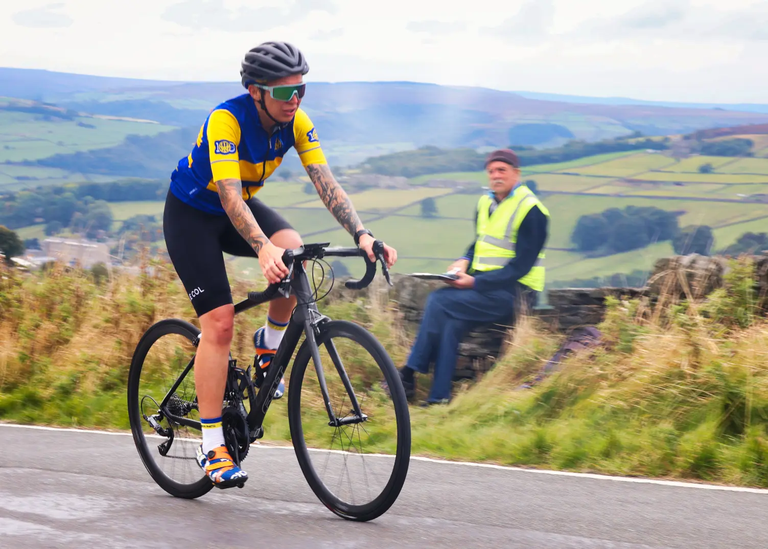A modern club rider on a Calderdale road with a marshal looking on